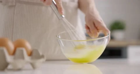 Process of mixing eggs with a whisk in a glass bowl on kitchen at home. Woman in Stock Footage 153085626