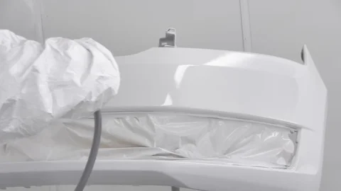The process of painting the bumper of a white car in a spray booth. Man using a Stock Footage 125884597