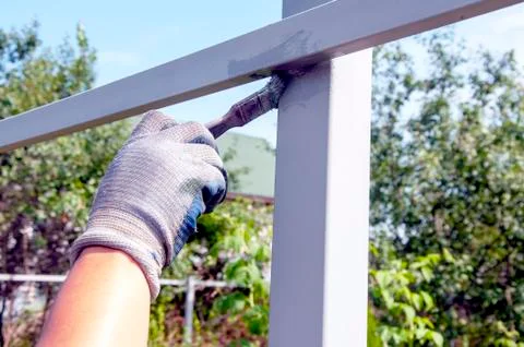 The process of painting rusty peeling rods on the fence. Man paints a brush w Stock Photos