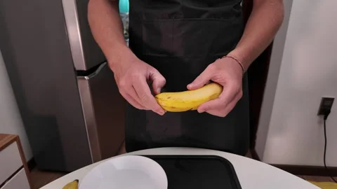 The process of peeling a banana. A mans hands peel a banana above a kitchen Stock Footage 318342884