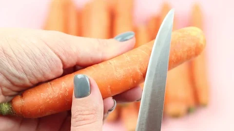 The process of peeling of carrot with a knife on pink background. Stock Footage 119889216