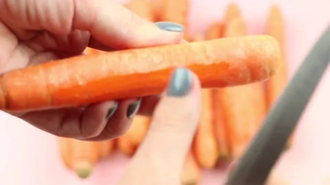 The process of peeling of carrot with a knife on pink background. Stock Footage