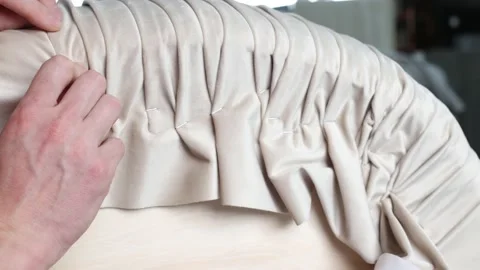 Process of pleating or draping beige fabric by hand on a furniture pouf Stock Footage 171004226