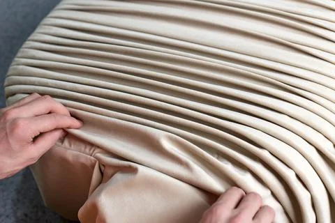 Process of pleating or draping beige fabric by hand on a furniture pouf Stock Photos