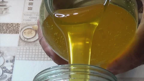 The process of pouring honey into a jar. Transfusion of yellow, sweet and Stock Footage 143376459
