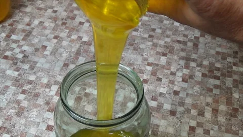 The process of pouring honey into a jar. Transfusion of yellow, sweet and Stock Footage 144094736