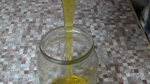 The process of pouring honey into a jar. Transfusion of yellow, sweet and Stock Footage 144510757