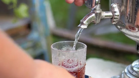 The process of pouring hot tea into a transparent glass from a metal samovar Stock-Footage 318555120