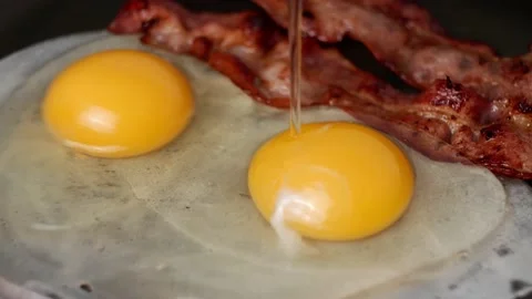 The process of pouring two eggs into a hot pan with fried bacon. Stock Footage 170321332