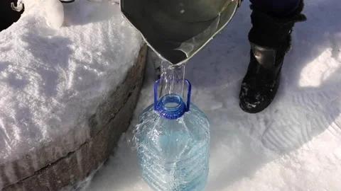 The process of pouring water from a well into a bottle in winter against a Stock Footage 148867519
