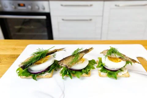 The process of preparing a festive snack on toast with sprats, onions, eggs and Stock Photos