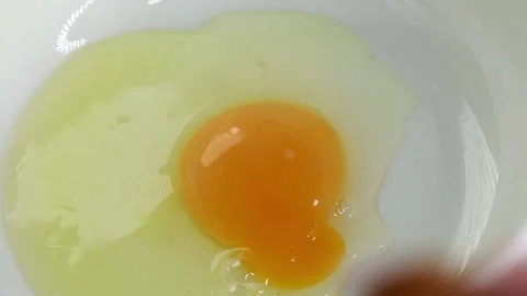 The process of preparing food for breakfast. Raw broken egg falling into white Stock Footage 161790721