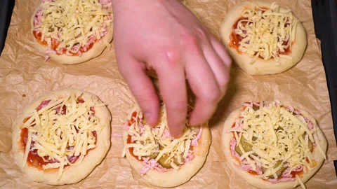 The process of preparing a mini pizza, adding grated cheese Stock Footage 249882714