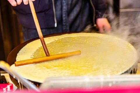 The process of preparing a pancake with a stick, which is leveled the dough.  Stock Photos