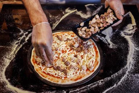 The process of preparing pizza, putting meat into it. Chef is wearing gloves. Stock Photos