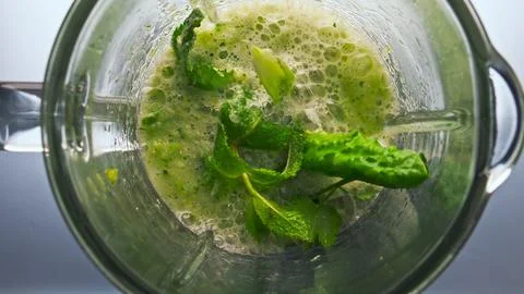 Process preparing smoothie in blender with veggies herbs fruits top view closeup Photos