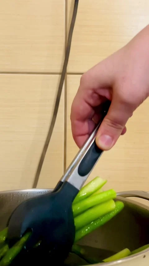 The process of pulling cooked green asparagus stalks with tongs in the kitchen Stock Footage 310409846