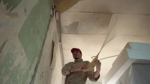 Process of removing old wallpaper from ceiling by man in uniform standing on Stock Footage 209290828