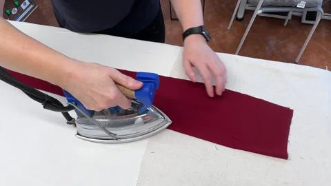 The process of sewing trousers. A hand presses an iron against a red piece of Stock Footage 296074753