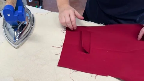 The process of sewing trousers. A hand strokes the seam of a tuck on a red cloth Stock Footage 296074736