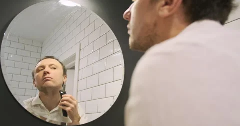 Process of shaving stubble with an electric trimmer. Reflection in the mirror Vídeo Stock 264019254