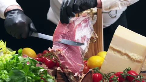 Process of slicing thin Italian or Spanish cured prosciutto with sharp knife for Stock Footage 302091102