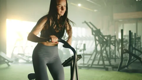 Process of training on air bike by athletic young woman in gym. Low angel shot Stock Footage 239545728