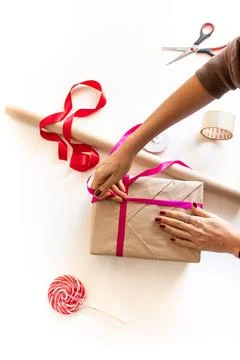 The process of wrapping a gift on a white table next to paper, ribbons, scissors Stock Photos