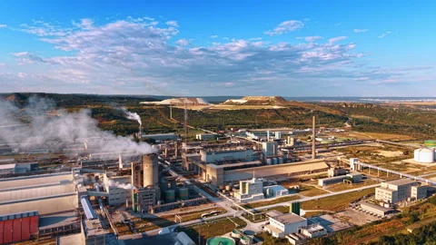 Processing factory below quarry mounds under blue sky. Steam rises from chimneys Stock Footage 339368054