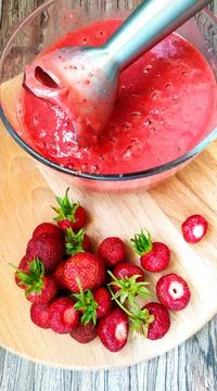 Processing strawberries with an electric blender. There is a cup of berry pur Stock Photos