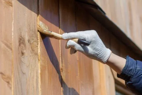 Processing of the wooden wall outside.A man's hand in a glove paint the woode Stock Photos
