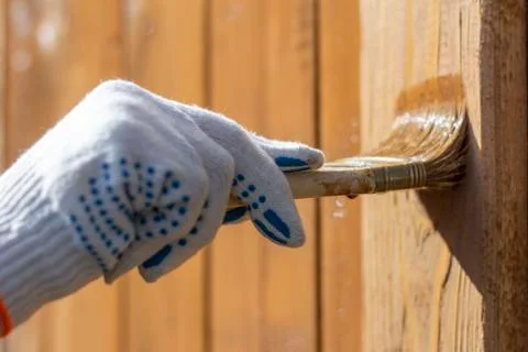Processing of the wooden wall outside.A man's hand in a glove paint the woode Stock Photos