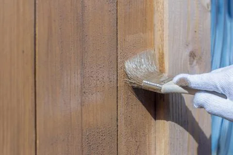 Processing of the wooden wall outside.A man's hand in a glove paint the woode Stock Photos