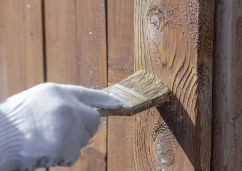 Processing of the wooden wall outside.A man's hand in a glove paint the woode Stock Photos