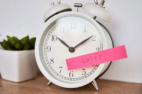 Procrastination and delay concept. Sticky note with word later on white alarm Stock Photos