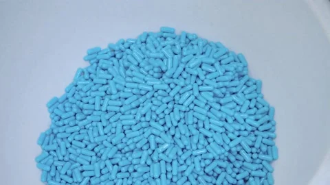 Produced blue capsules falling down to the container. close-up of pills Stock Footage 200856360