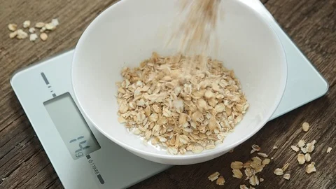Product weighing concept. Man pours oatmeal into a white bowl on the kitchen Stock Footage