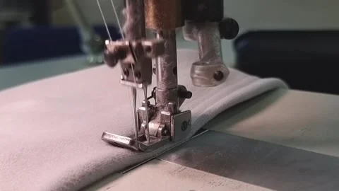 A production flat-seam machine makes a close-up stitch on a gray fabric. Stock Footage 315409903