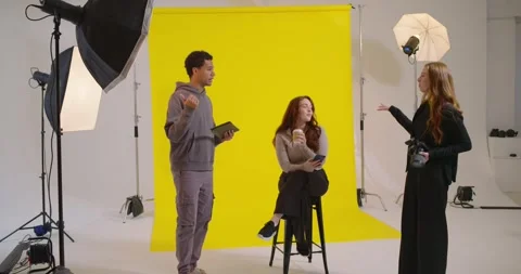 Production team using moodboard, directing seated female model on yellow 스톡 동영상 347408593
