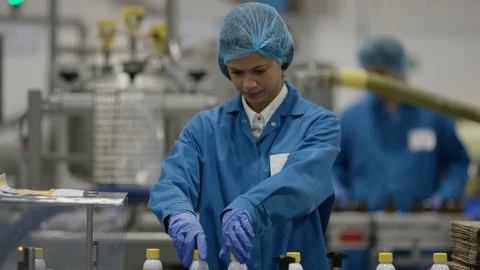 Production worker arranging bottles on conveyor belt at cosmetic factory Stock Footage 107996492