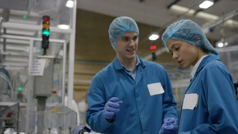 Production worker inspecting cosmetic bottles moving on conveyor belt Stock Footage 107974161