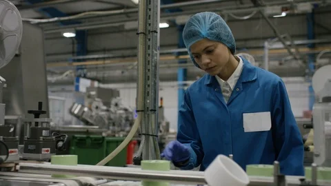 Production worker inspecting packed cosmetic boxes on conveyor belt in factory Stock Footage 107957480