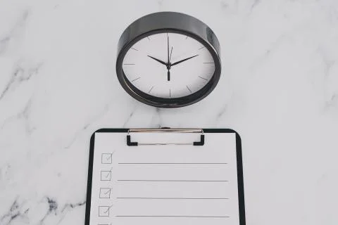 Productivity and deadlines, to do list on clipboard next to big clock on busi Stock Photos