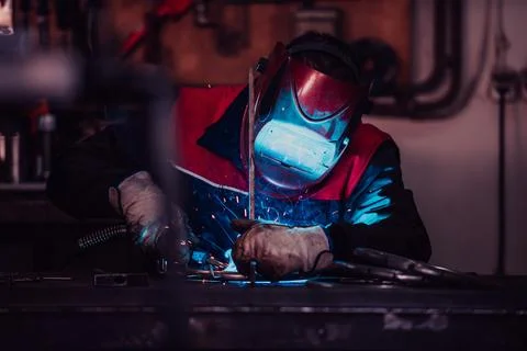 Profesional welder in protective uniform and mask welding metal pipe on the Foto stock