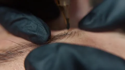 Professional aesthetician performing microblading on a client's eyebrow, using a Stock Footage 331575731