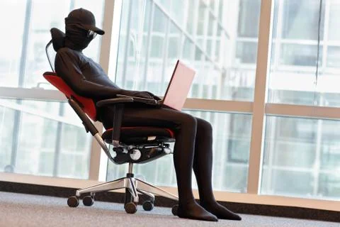 Professional anonymous hacker working with laptop in office Stock Photos