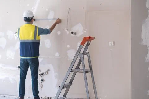 Professional architect in protective hardhat measuring wall standing near ladder Stock Photos