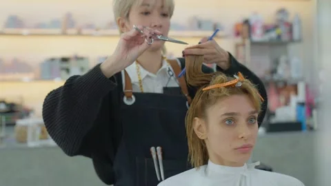 Professional Asian barber using scissors and comb to cut their caucasion, whi Stock Footage 153953089