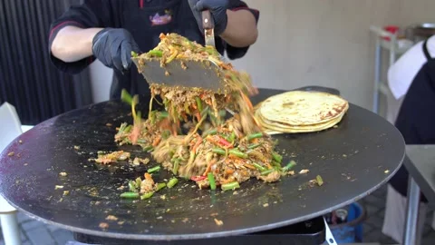 A professional Asian chef stirring lamb curry on a large flat frying pan Stock Footage 210417098