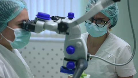 Professional assistant adjusting dental microscope as blurred dentist examining Vídeos de archivo 201220296